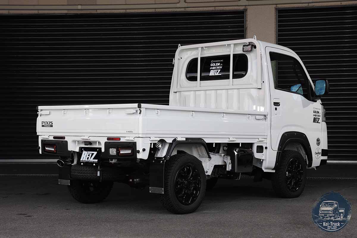 White kei truck viewed from the rear and side in front of a dark garage shutter.