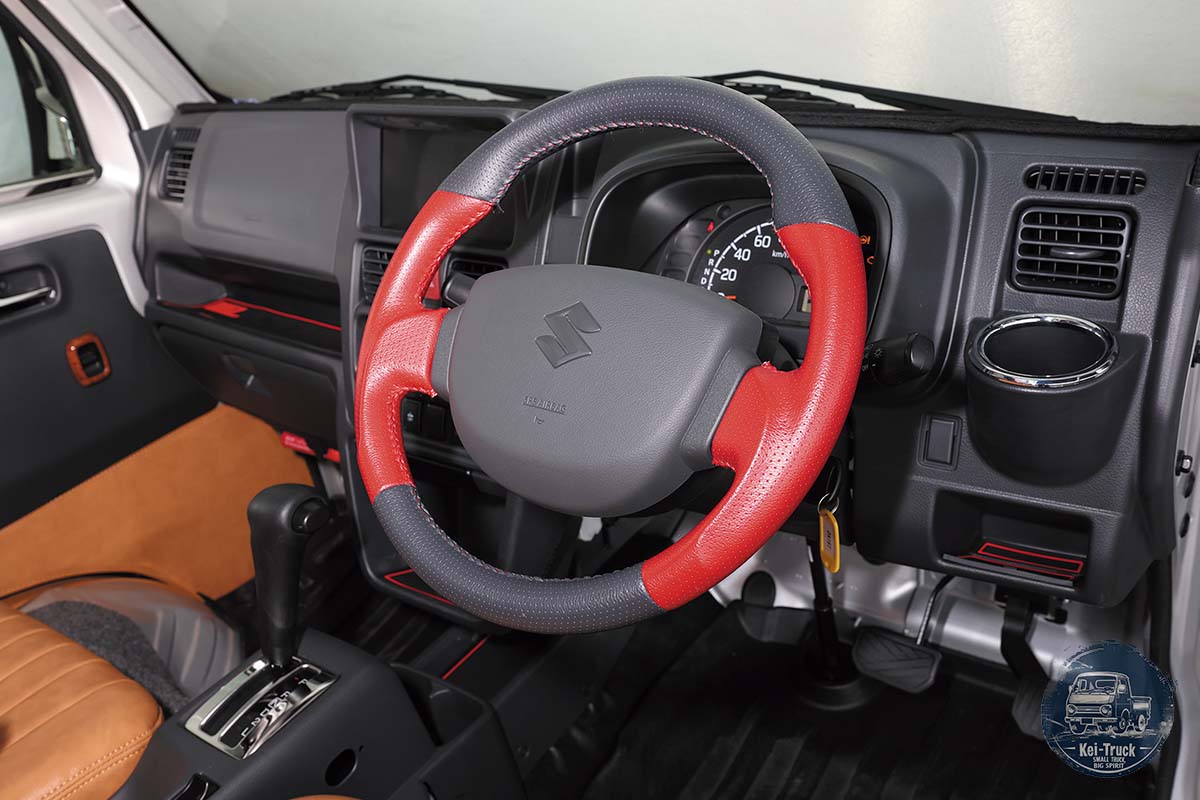 Red-and-black steering wheel and dark dashboard inside a kei truck.