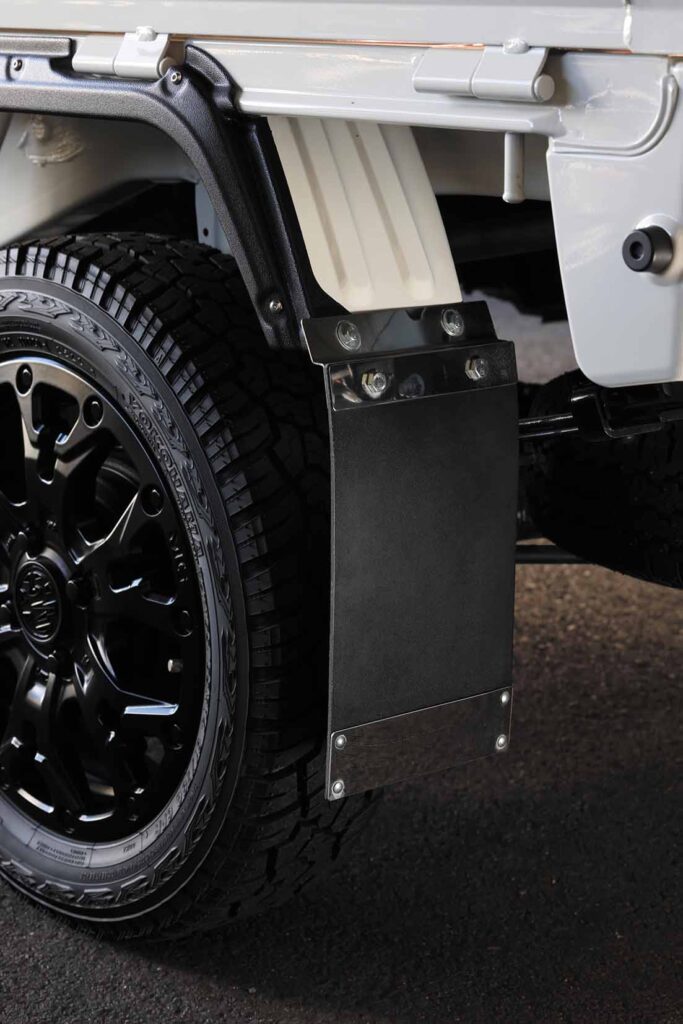 Close-up of a white kei truck rear wheel with aggressive mud-terrain tire, black multi-spoke alloy wheel and rubber mud flap