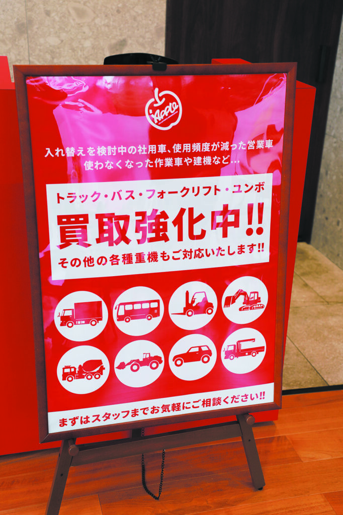 Red Japanese dealership poster advertising vehicle buyback service for trucks, buses, forklifts and excavators showing strong demand for used commercial vehicles in Japan

