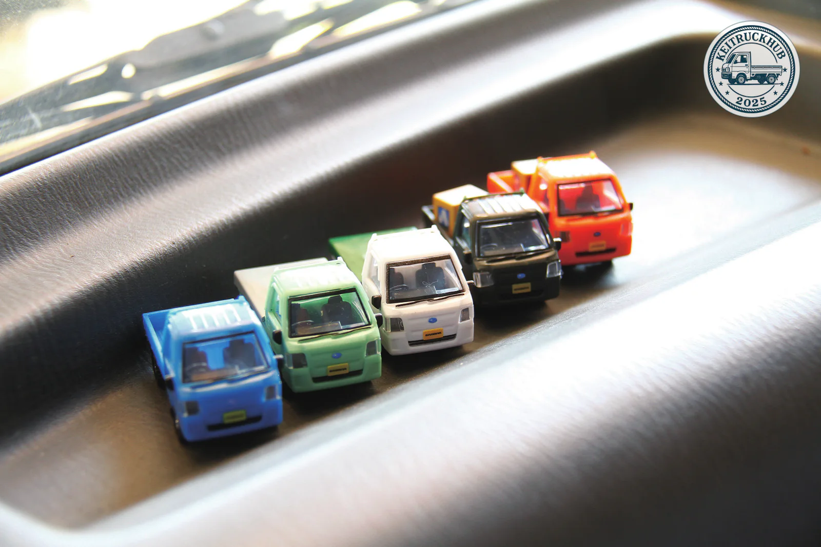 Five miniature Subaru Sambar trucks in different colors lined up on a dashboard.